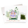 "Gathering Moss" New Home Card features a little baggie of real moss beside an charming, casually illustrated home. Message on the front says: "A rolling stone gathers no moss"